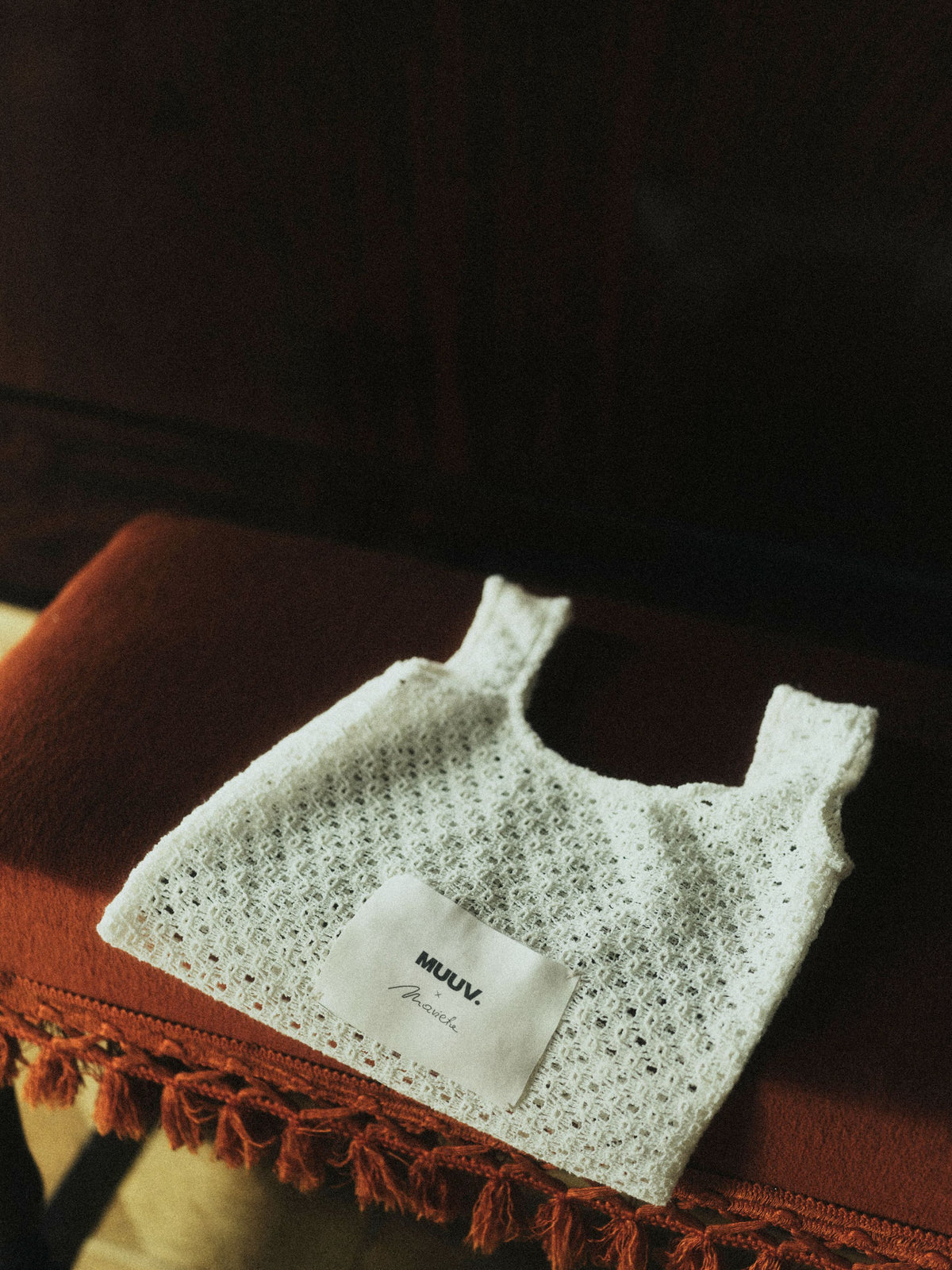 Koronkowa mini torba ORIA off-white z kolekcji Mariety Żukowskiej dla Muuv, prezentowana na czerwonej sofie, dostępna na beetles.shop.