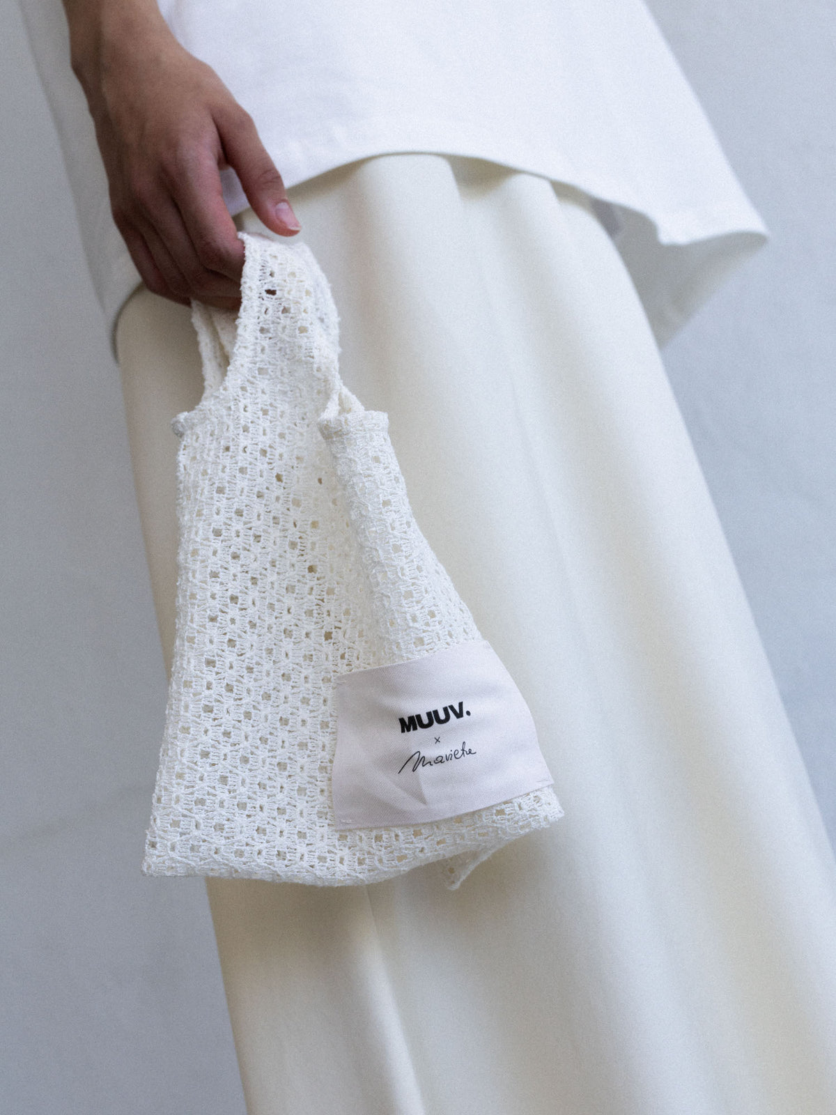 Mini torba ORIA off-white z ażurowej koronki, trzymana w dłoni, z naszywką Muuv x Marieta Żukowska, dostępna na beetles.shop.